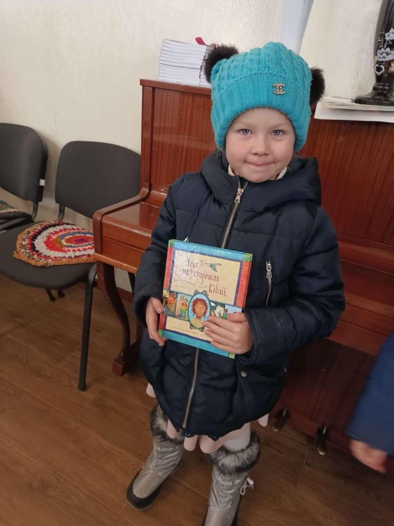 A young girl in a woollen hat and thick coat holding the Jesus Storybook Bible she has been given