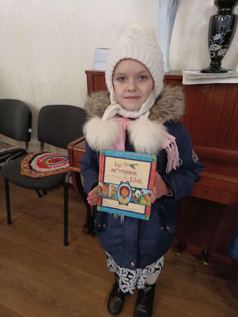 A young girl in a woollen hat and thick coat holding the Jesus Storybook Bible she has been given