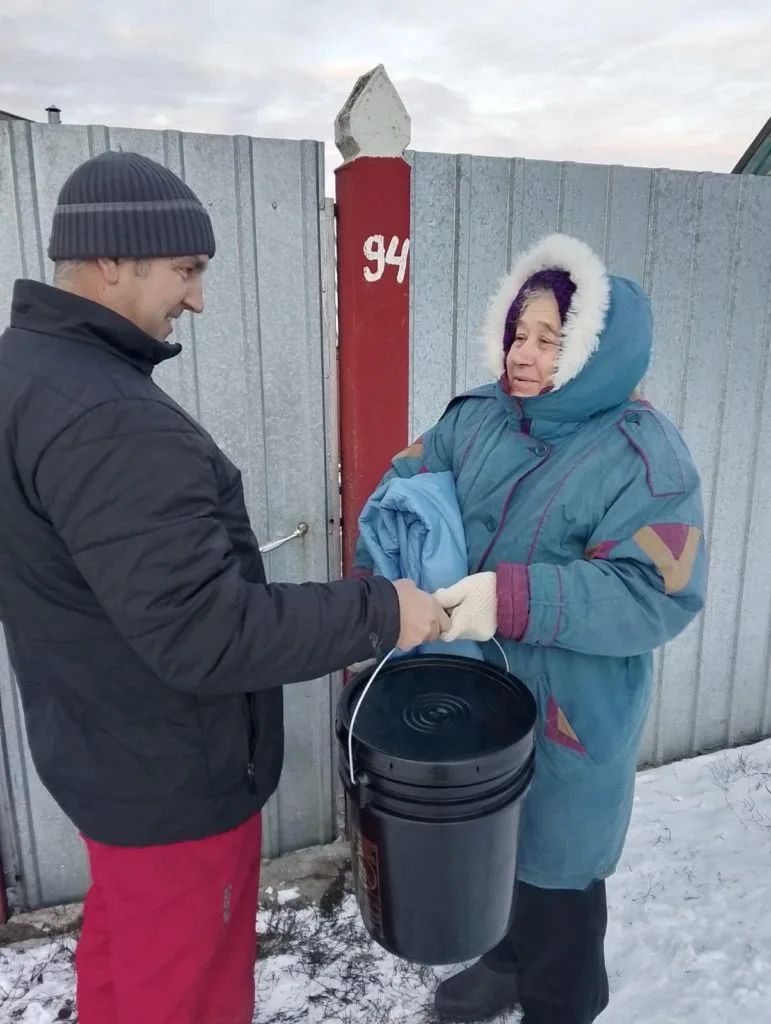 Pasotr Andrew passing a bucket of aid to an elderly lady who is also holding some donated bedding