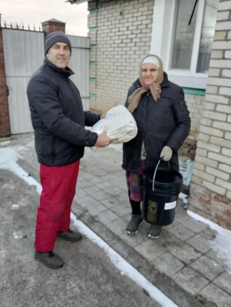 Pastor Andrew handing an elderly lady some donated bedding.  She is also holding a bucket of donated aid