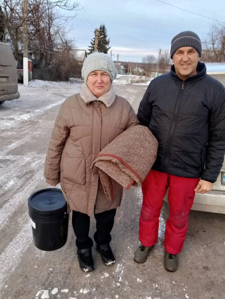 Pastor Andrew standing next to a lady holding a bucket of donated aid standing outside in thick winter clothing