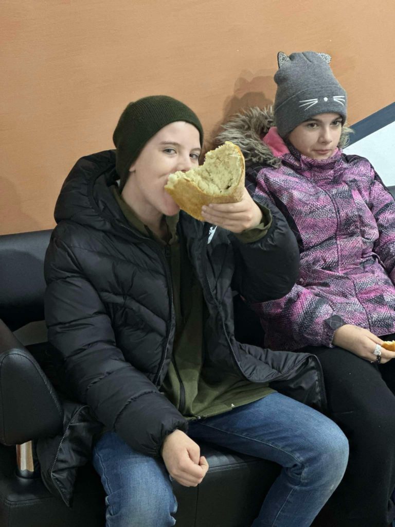 A boy who is sat down, munching on a whole fresh loaf of bread