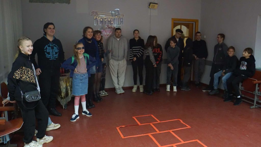 Bohdan, the team and the children standing at one end of a room against a wall looking towards the opposite end