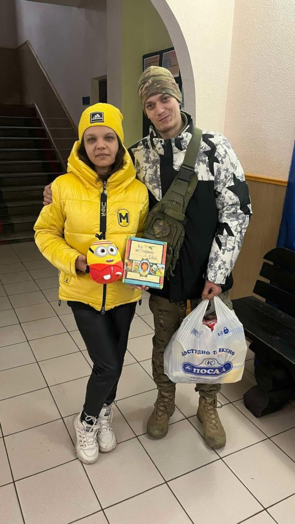 Igor standing with his wife who is holding a copy of the Jesus Storybook Bible and a cuddly minion toy.