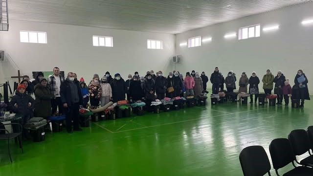 Refugees standing in the Sports Hall at the Centre lined up with the aid they have been donated