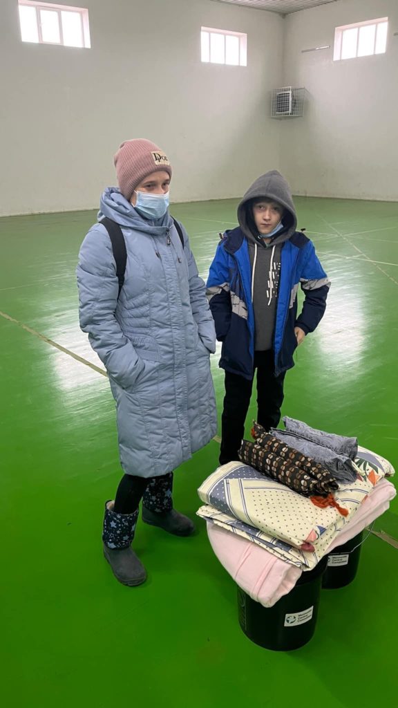 A woman and a boy standing in the Centre in front bedding and other aid.