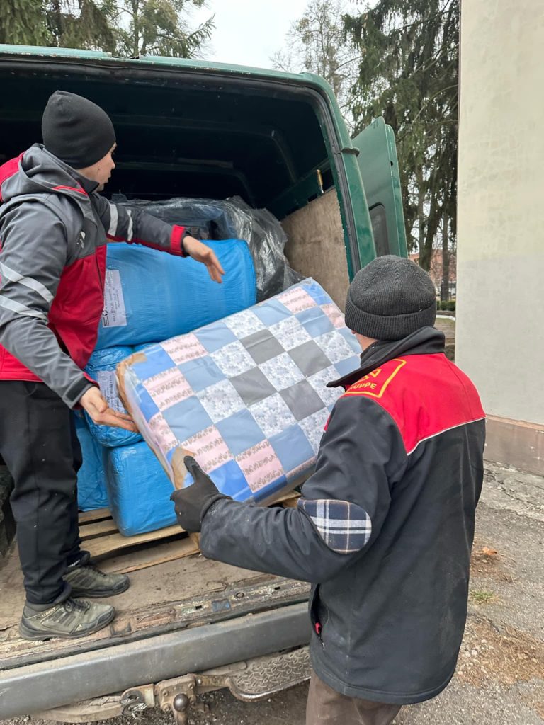 A man passing packs of blankets from the back of a van to another man on the ground.