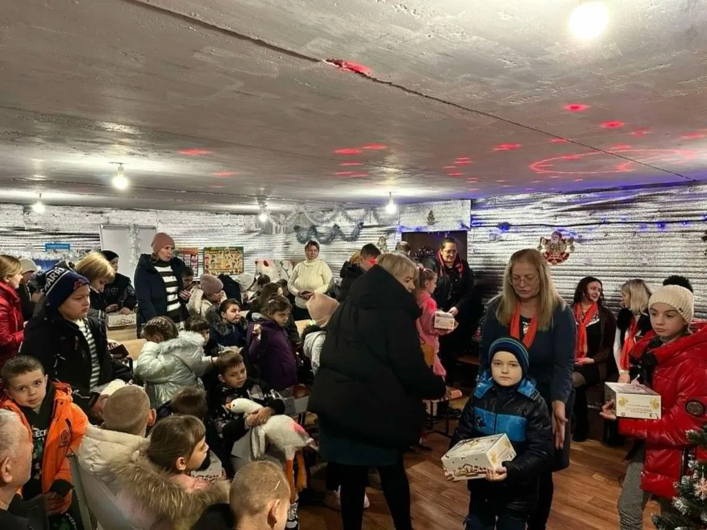 An underground bomb shelter with a low ceiling, full of children holding presents donated to them