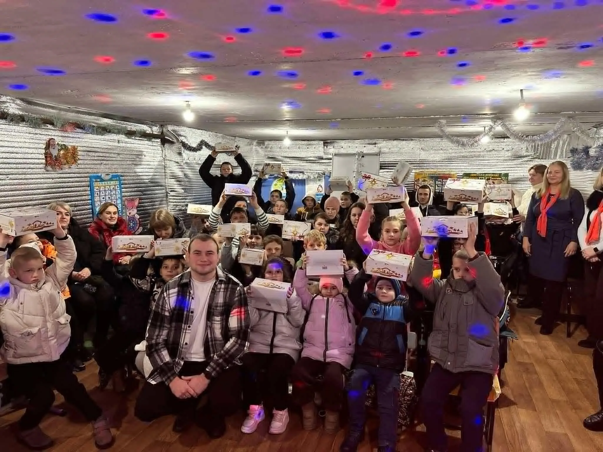 An underground bomb shelter with a low ceiling, full of children holding presents above their heads donated to them