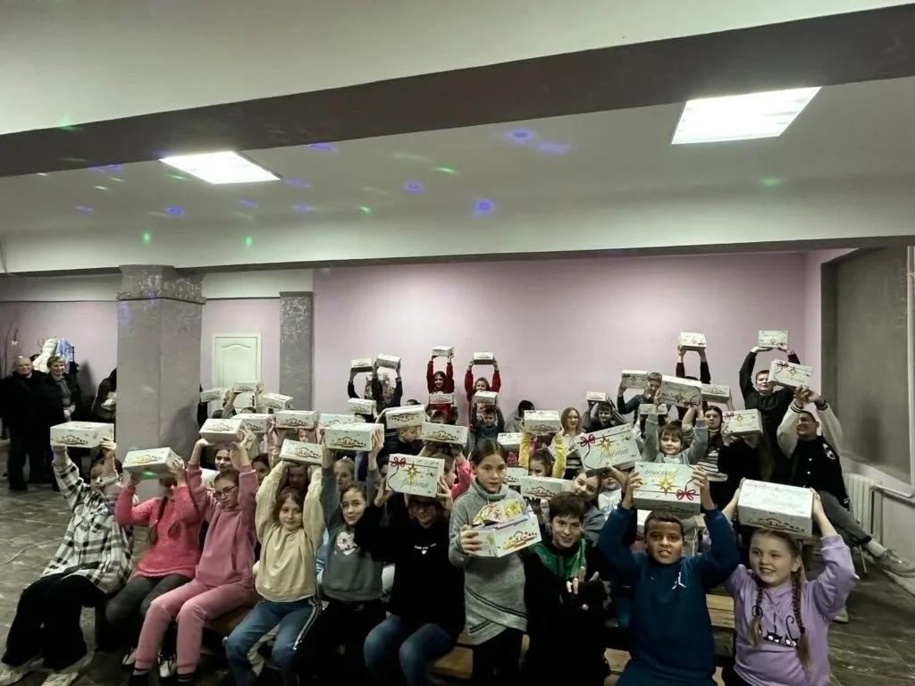 An underground bomb shelter with a low ceiling, full of children holding presents above their head donated to them