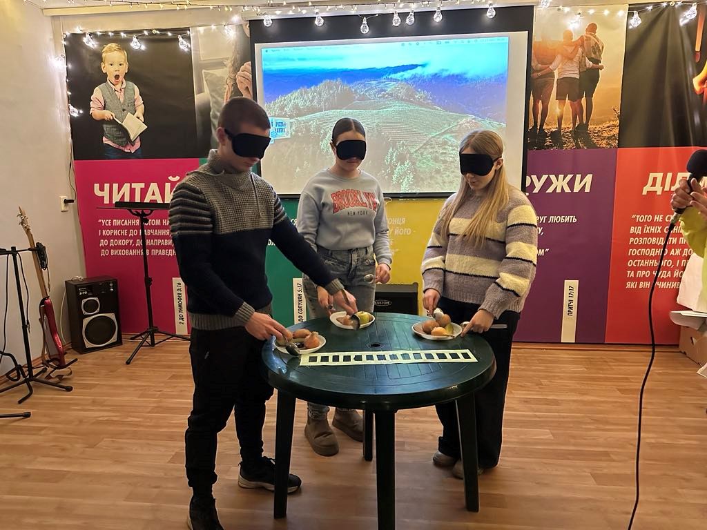 Three of the youth group standing, blindfolded, at a table playing a game