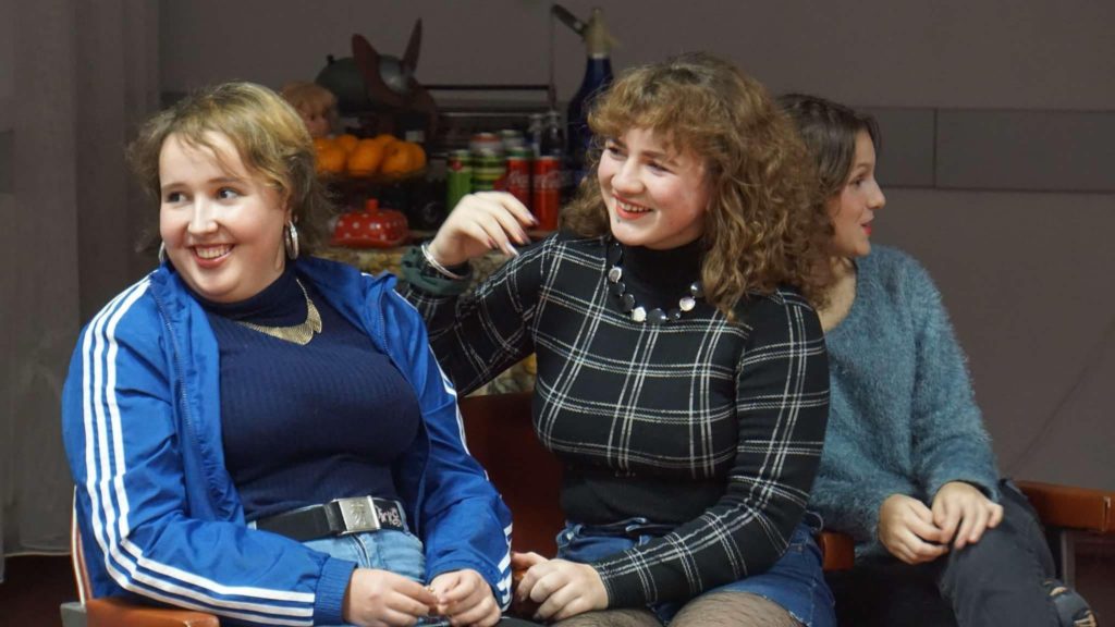 Two of the female youth sat down talking to someone out of shot and smiling