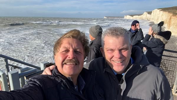 A selfie of Sergey Rakhuba and Peter Martin standing in windy weather with the stormy sea and white cliffs behind them