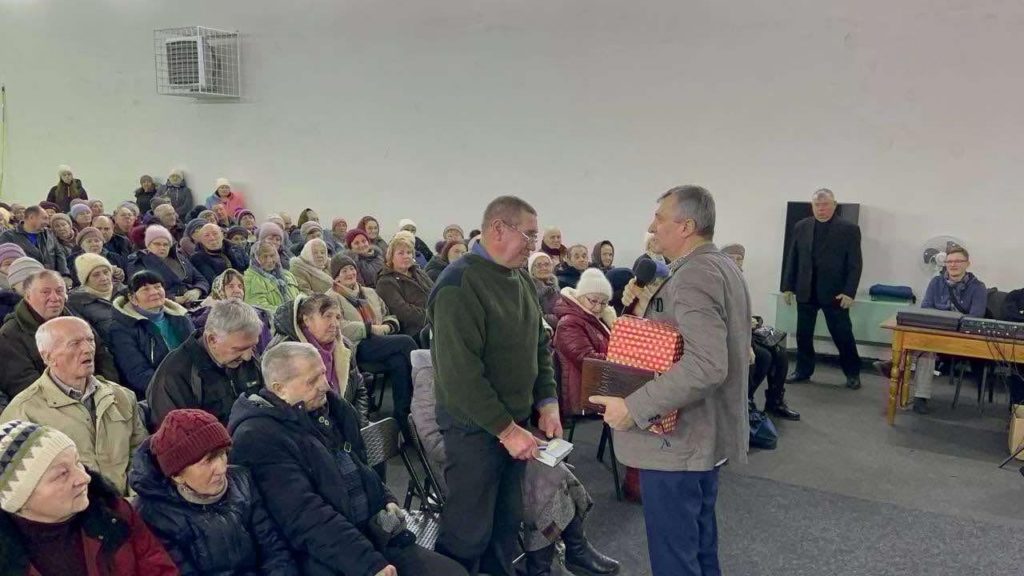 A man in the front row of the service at the Centre, standing with a Bible in his hands whilst being spoken to by the speaker