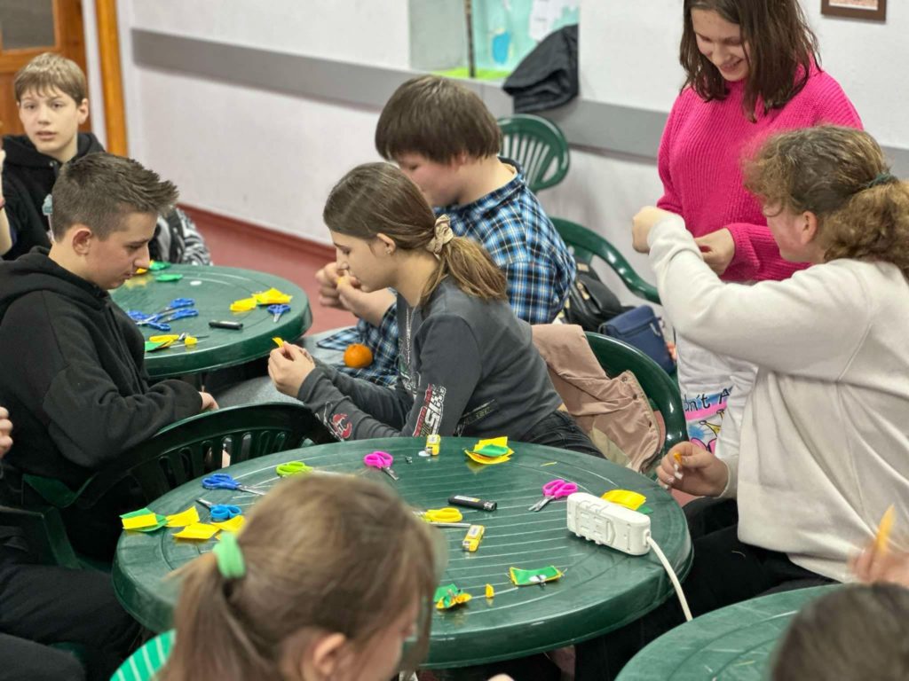 Children during the winter camp sitting at three round plastic garden tables doing crafts.