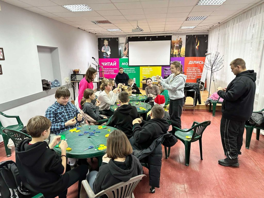 Children during the winter camp sitting at three round plastic garden tables doing crafts.