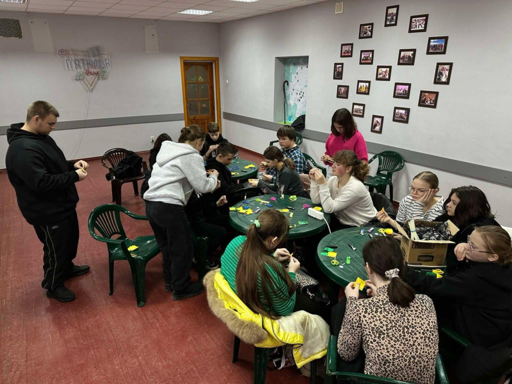 Children during the winter camp sitting at three round plastic garden tables doing crafts.