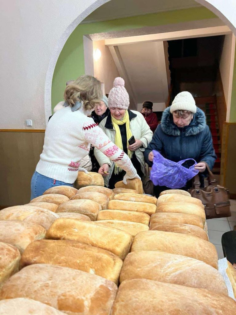 Loaves of bread piled on a long table with people queuing at the far end to collect them