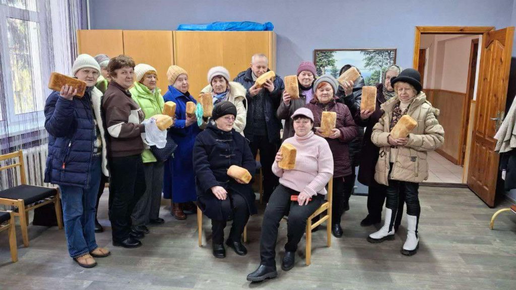 A group of about 20 people standing and sitting in the Centre holding loaves of bread they have collected