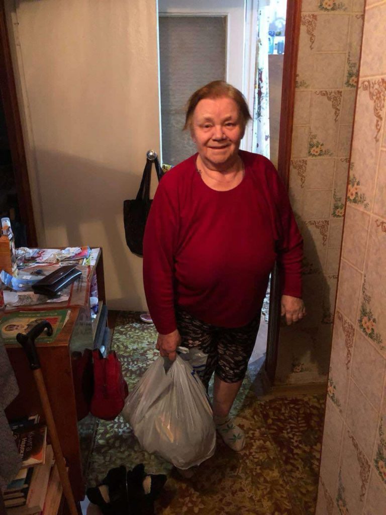 A lady standing in her living room holding a plastic bag of donated aid