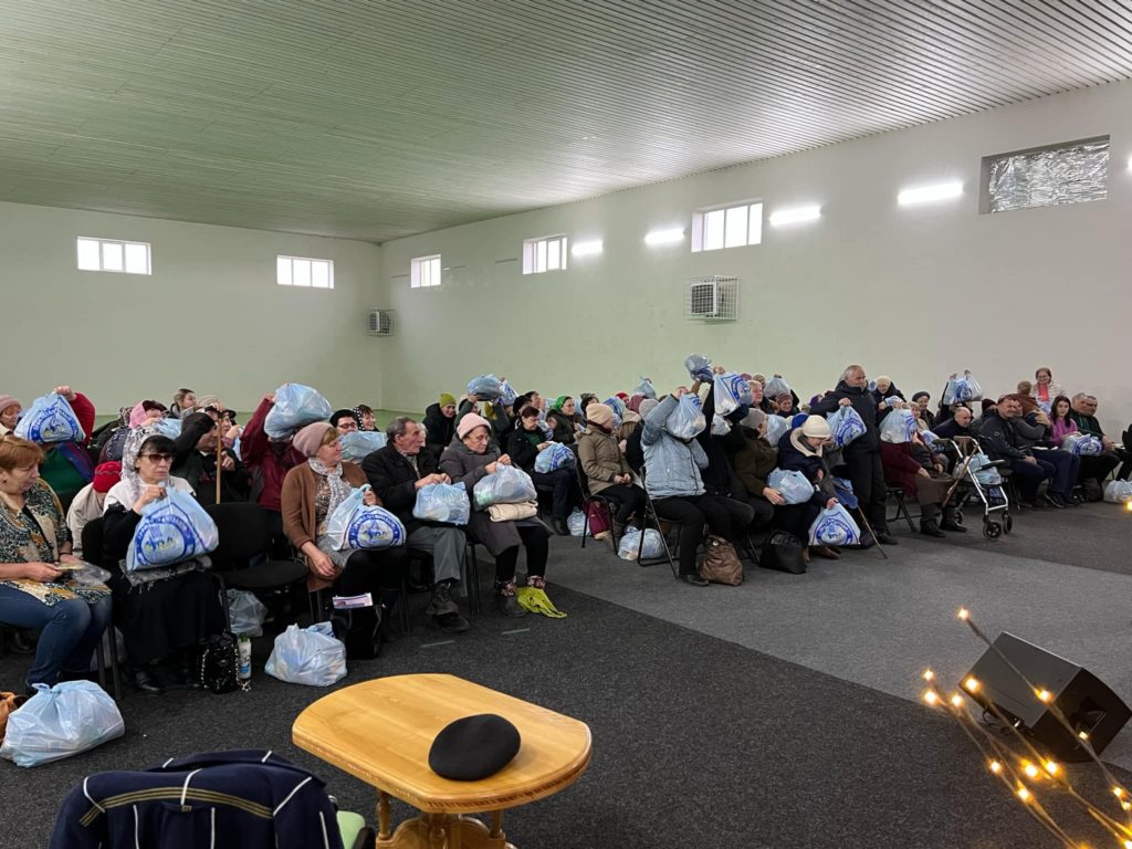 People sat in rows of chairs in the hall at the Centre with plastic bags of donated aid.