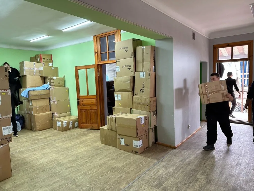 Boxes of aid stacked inside a room piled up to the ceiling with a man carrying another box in from outside