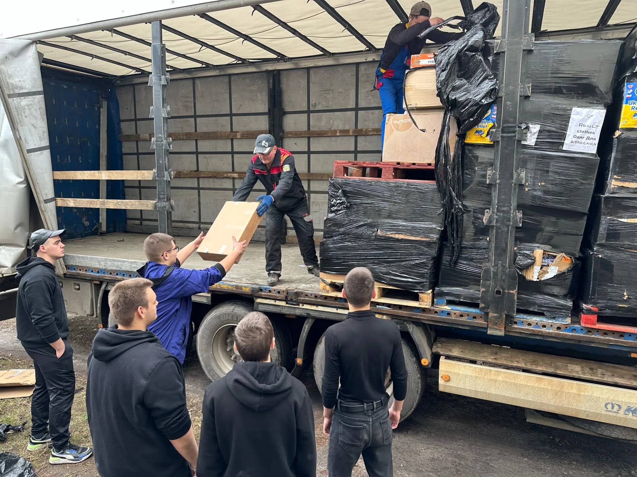 Aid being unloaded from a curtain sided truck with packages being passed down to people waiting on the ground
