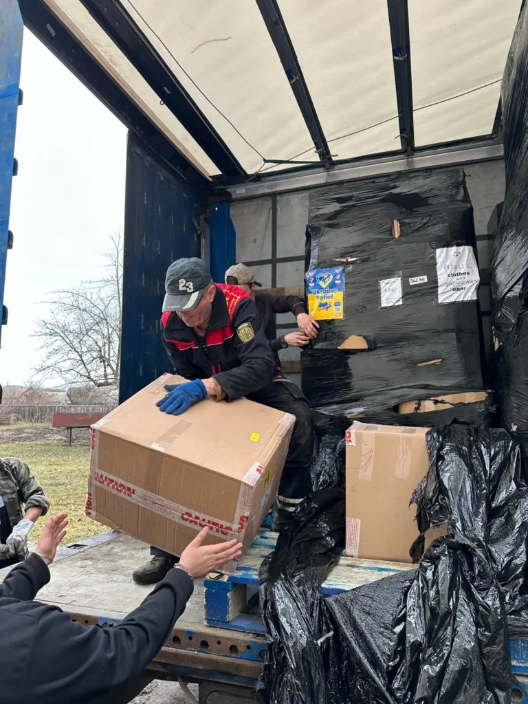 Aid being unloaded from a curtain sided truck with packages being passed down to people waiting on the ground