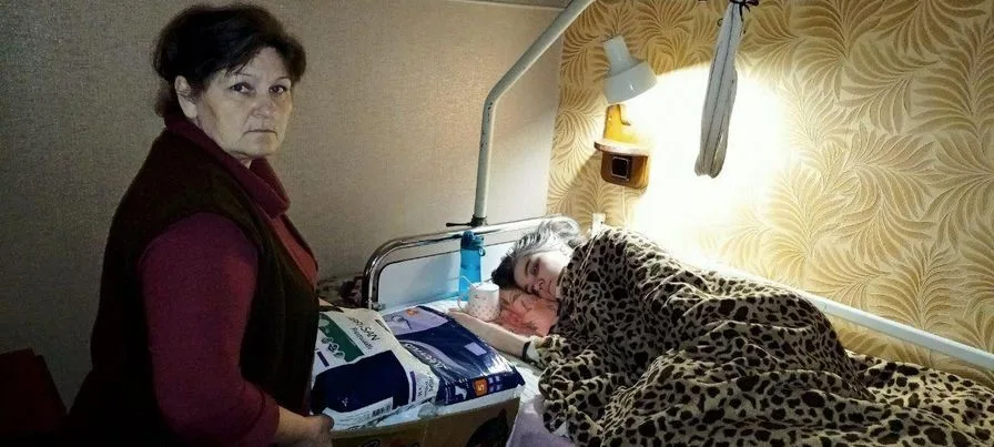 Ludmilla standing next to her daughter Natahsa laying in a hospital bed