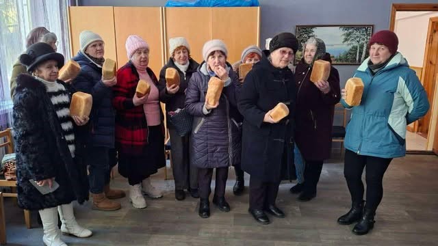 A group of 10 ladies holding up loaves of bread they have collected