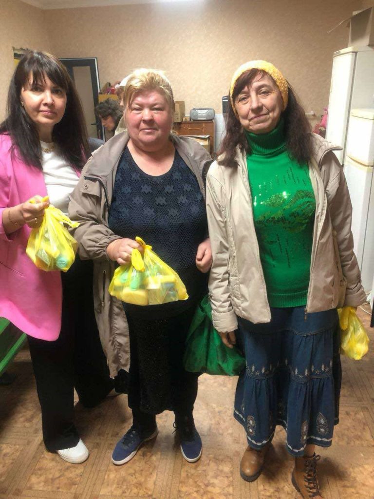 Three ladies stood indoors holding bags of aid