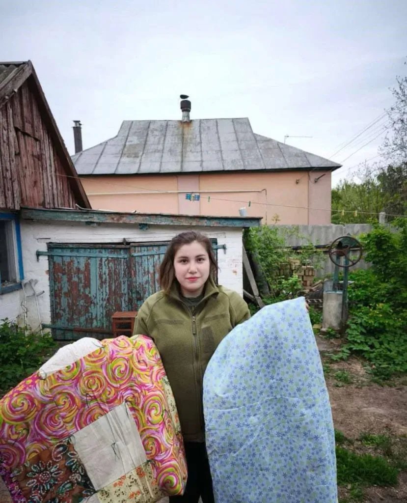 A lady stood in the garden of her home holding two donated quilted blankets