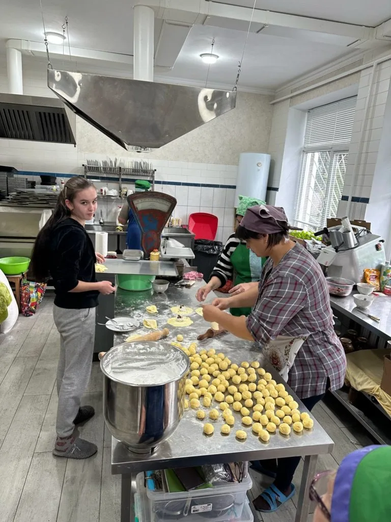 Bakers hard at work in the bakery working with dough, with balls of dough spread across the stainless steel work table