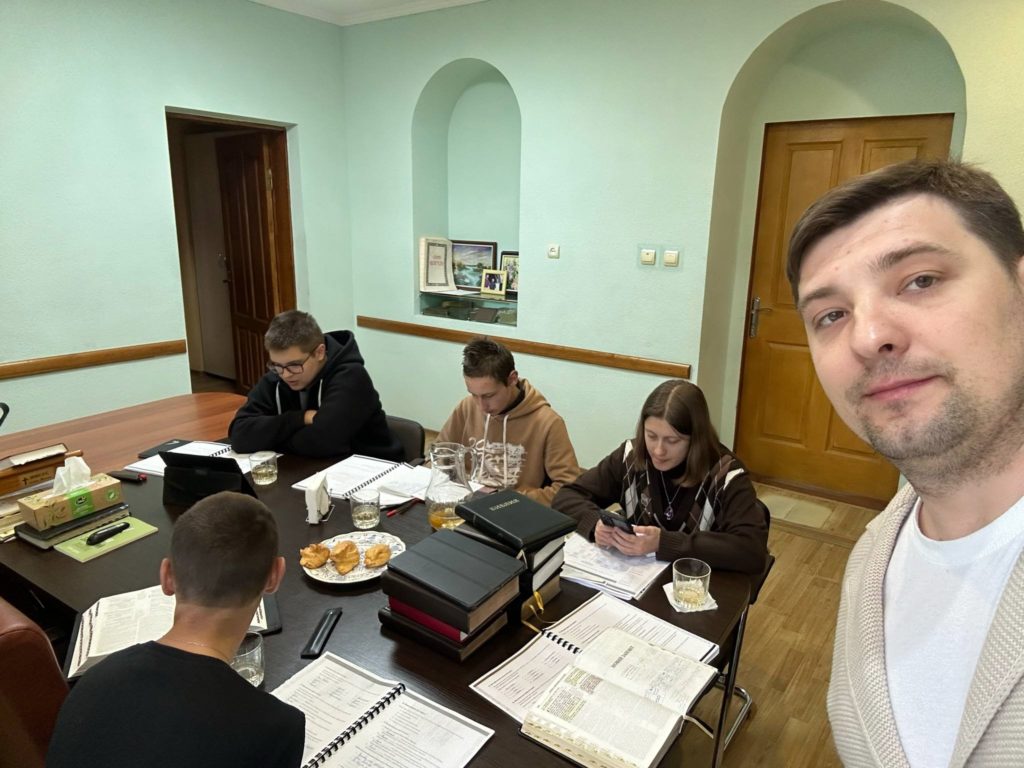 Bohdan taking a selfie with youth doing their baptismal class sat around a table with books and Bibles open