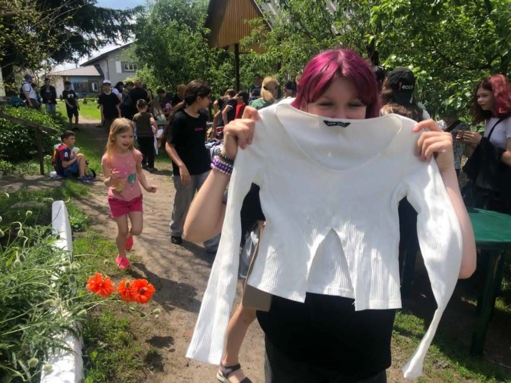 A teenage girl holding up a white long sleeved top that she has picked up from the piles of donations