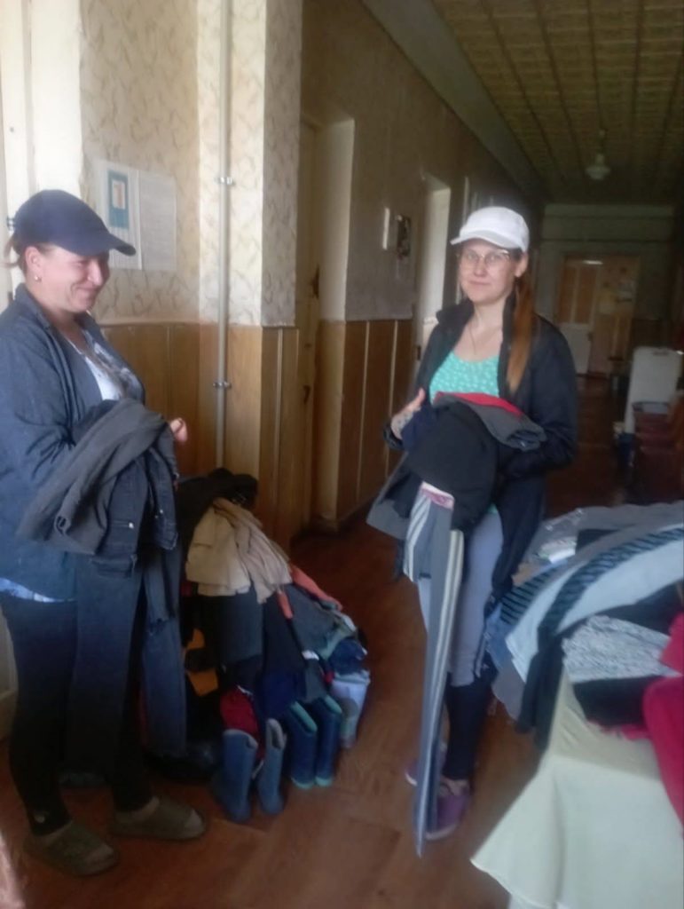 Two ladies standing in a corridor with donated clothes draped over their arms