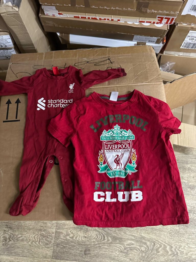 A Liverpool FC baby grow and t-shirt laid out on top of a cupboard box