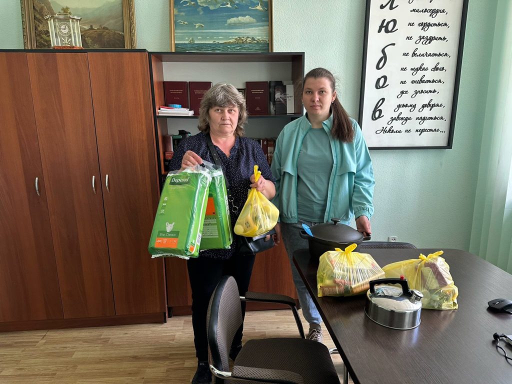 Two ladies stood next to a desk in an office holding bags of donated aid