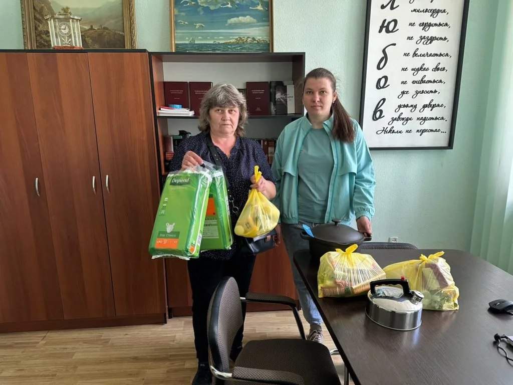 Two ladies stood next to a desk in an office holding bags of donated aid