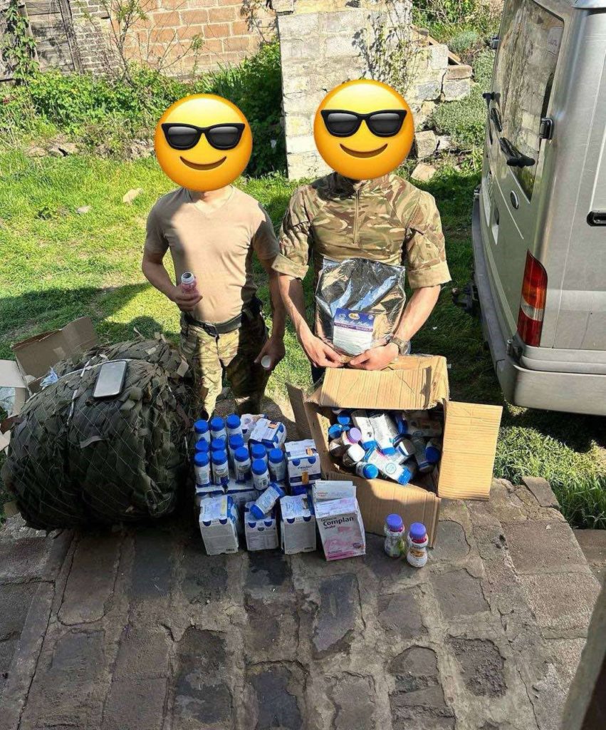 Two soldiers with their faces obscured with donated bottles of energy drinks piled in front of them
