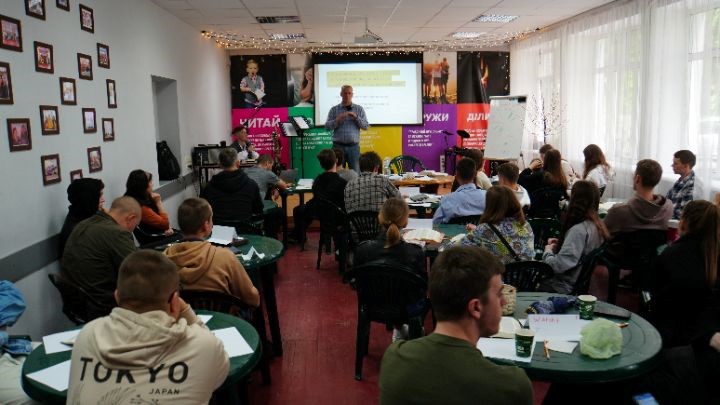 Youth sat around tables in a seminar with the speaker standing at the front