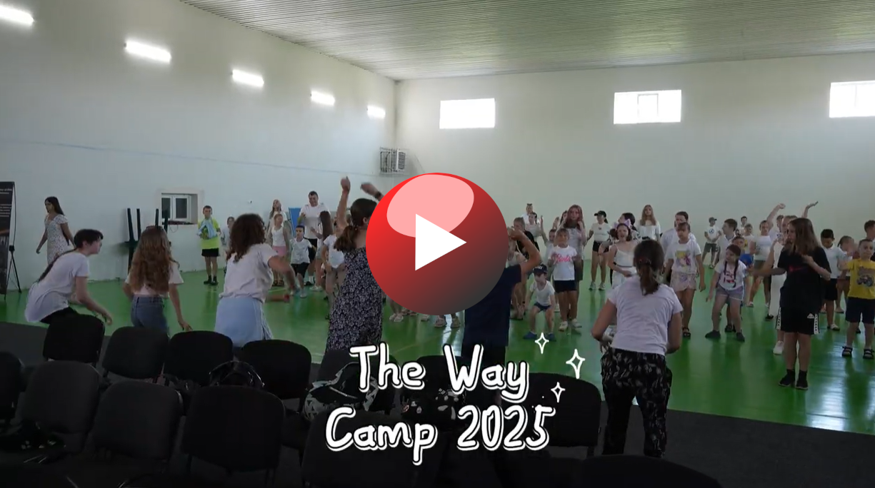 Children and leaders enthusiastically dancing in a large indoor gym with the text “The Way Camp 2025” overlaid, and a red play button indicating a video thumbnail.