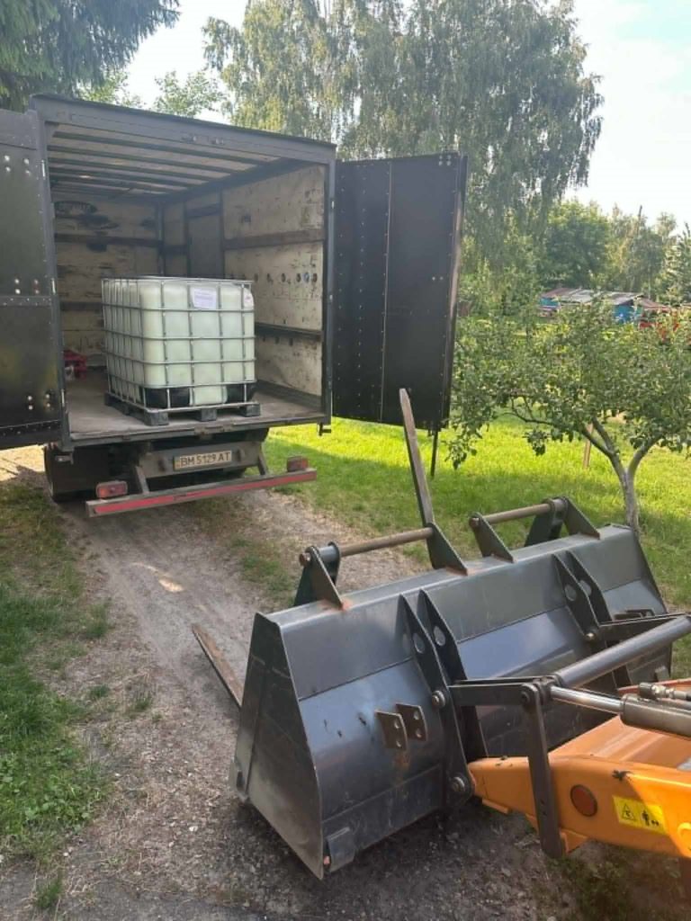 A forklift prepares to unload a large container from the back of a truck parked on a dirt path