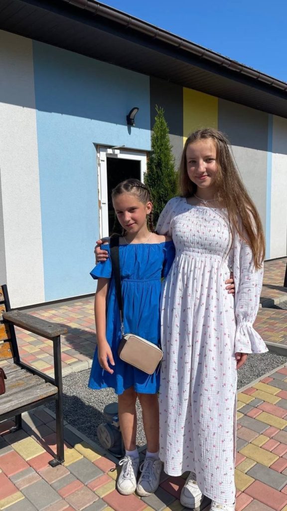 Two girls dressed in summer dresses standing outside a colourful building on a sunny day