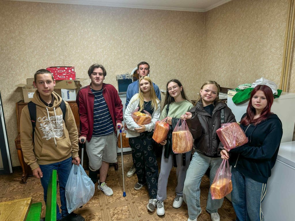 Group of young people holding bags filled with loaves of bread, smiling and standing together.