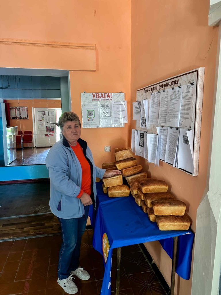 Woman standing next to a table stacked with loaves of bread inside the Centre.