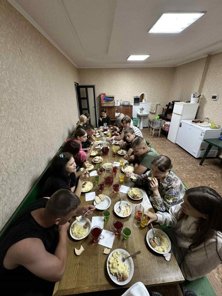 Overhead shot of young people at a long table eating dinner, with plates of food and colourful drinks.