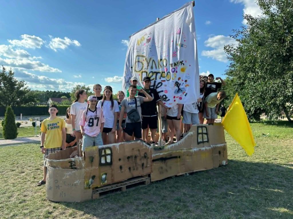 Youth group standing inside a cardboard boat structure with a large painted sail, smiling at the camera.