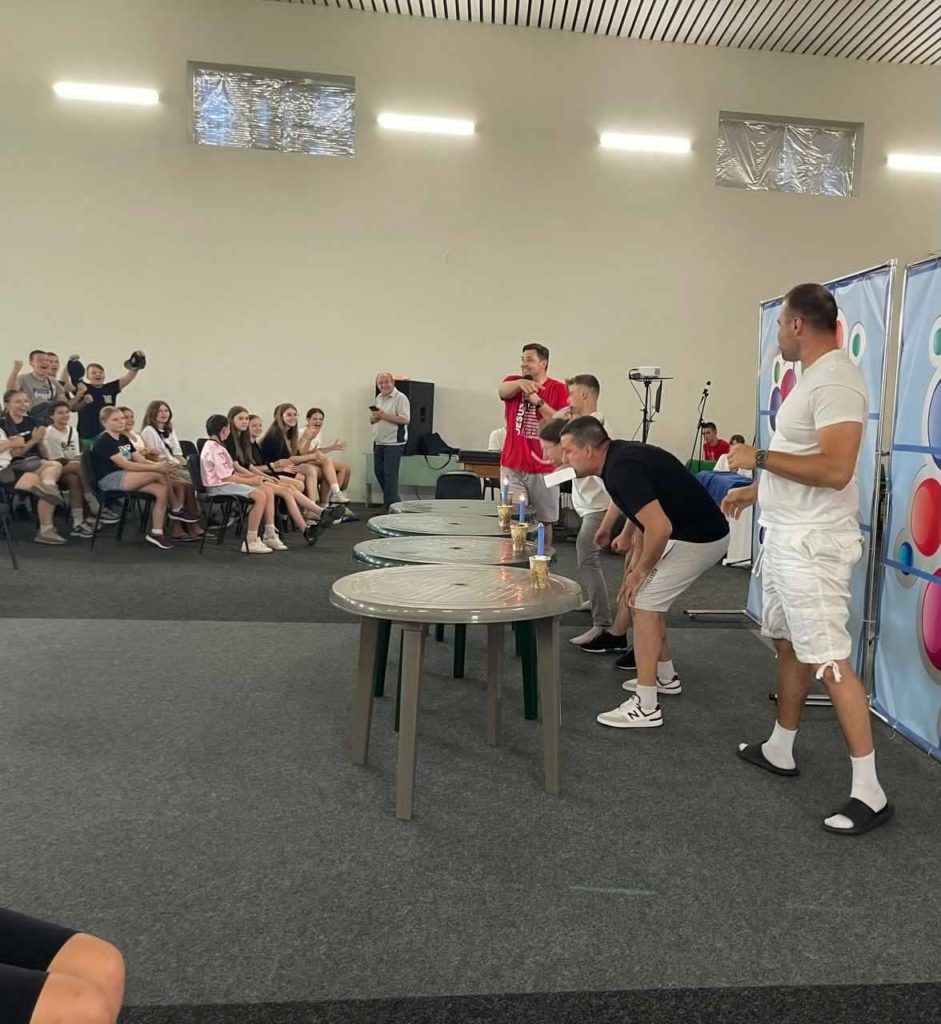 Camp participants indoors, engaged in a fun competition using cups and candles on plastic tables.