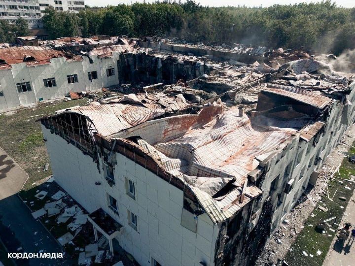 Aerial view of a heavily damaged university building with a collapsed roof and debris scattered around after a bombing.
